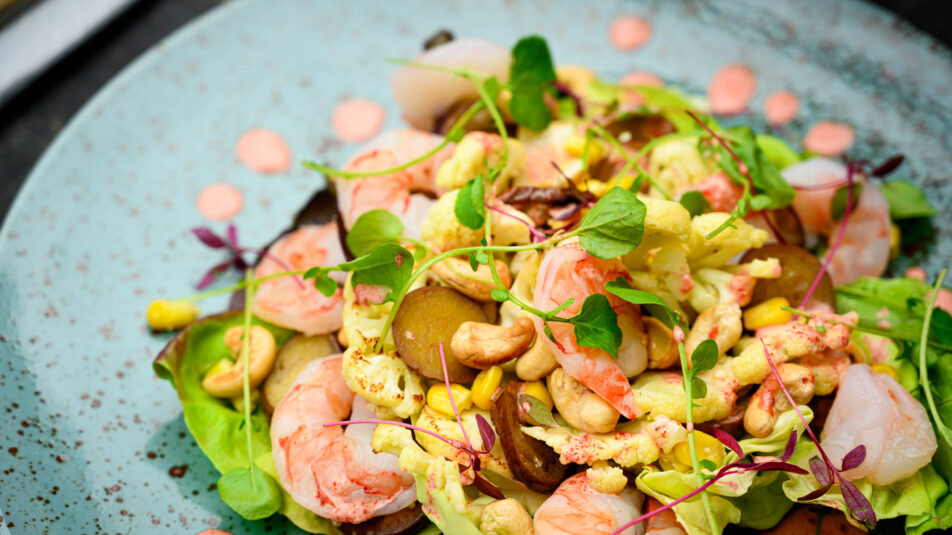 Auberginen-Blumenkohlsalat mit Crevetten, angerichtet auf Salatblättern.