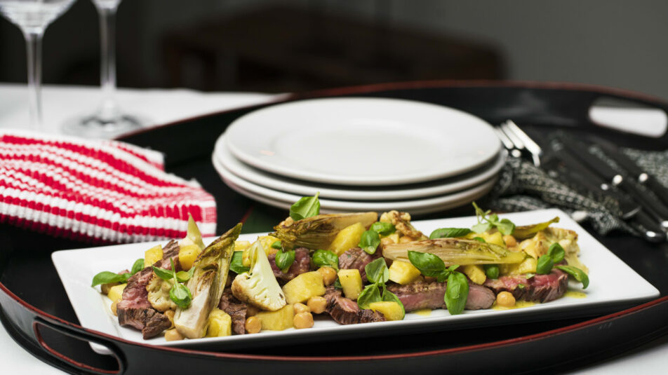 Dunkler Teller mit Flanksteak und Chicorée-Salat, elegant angerichtet