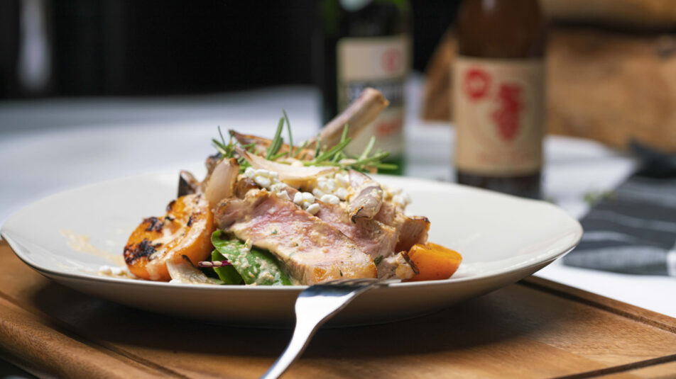 Teller mit Kalbskotelett und Aprikosensalat, eine Gabel ist an den Teller gelehnt