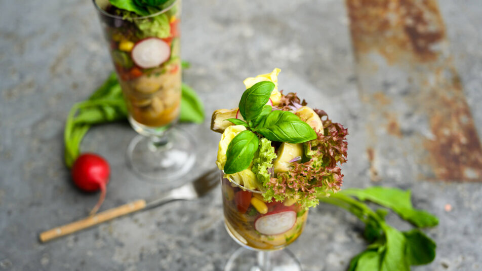 Pasta-Gurken-Mais-Salat im Glas angerichtet, auf einem Granittisch serviert.