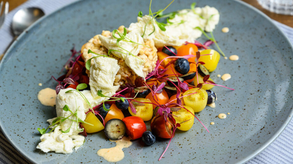 Auf einem leicht bläulichen Teller ein Salat aus Tomaten und Gerste, frisch und farbenfroh angerichtet