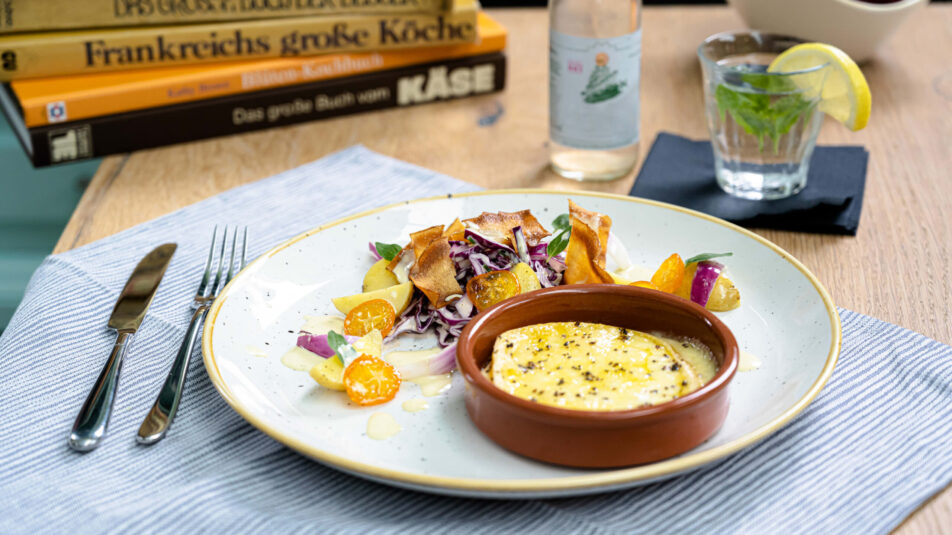 Winterhafter Salat mit einer Scheibe Raclette-Käse daneben.