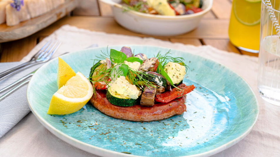 Grillierte Wurst mit würzigem Ofengemüse und Brunos Kräuterbutter, garniert mit frischen Kräutern.