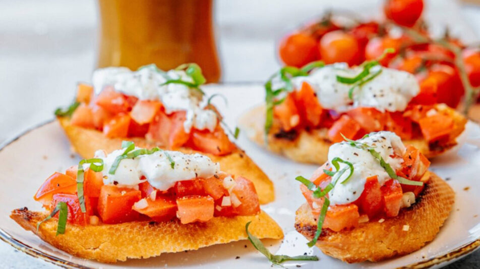 Bruschetta mit Burrata und Tomaten. Im Hintergrund eine Flasche Brunos Salatsauce Italienisch.