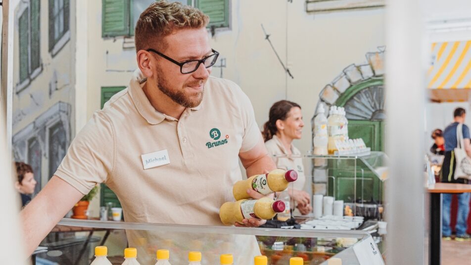 Bruno's Best Mitarbeiter mit mehreren Flaschen Salatsauce am Messestand vor einer Auslage mit bunten Saucenflaschen