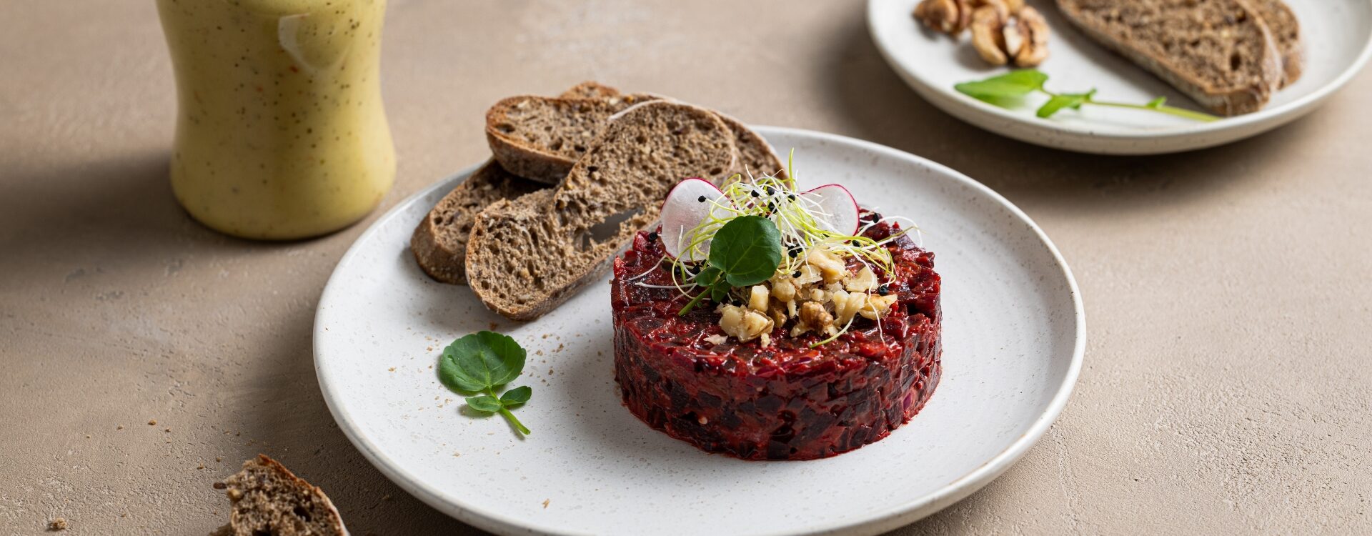 Randen-Tatar angerichtet auf einem Teller. Im Hintergrund eine Flasche Brunos Salatsauce Vinaigrette und Brot.