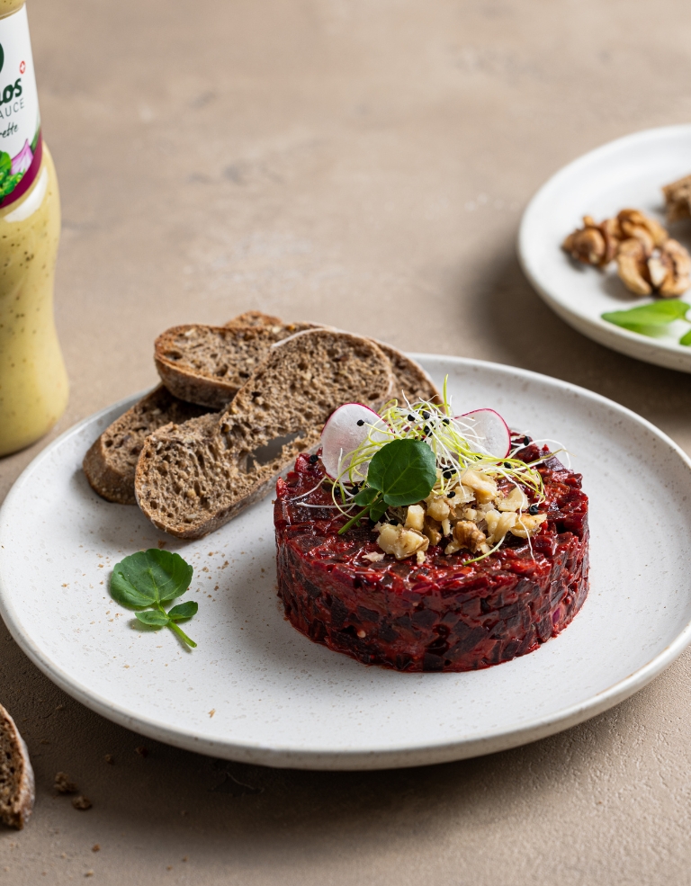 Randen-Tatar angerichtet auf einem Teller. Im Hintergrund eine Flasche Brunos Salatsauce Vinaigrette und Brot.