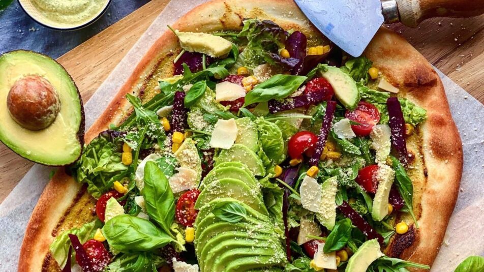 Vegane Salat-Pizza mit Avocado auf einem Holzbrett.
