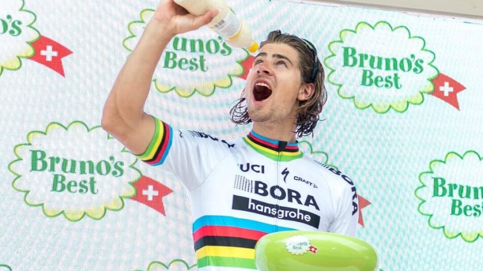 Radfahrer Peter Sagan auf dem Podium der Tour de Suisse mit einer Flasche Brunos Salatsauce Französisch in der einen Hand und einer Salatschüssel in der anderen, daneben ein lächelnder Mitarbeiter der Bruno's Best AG