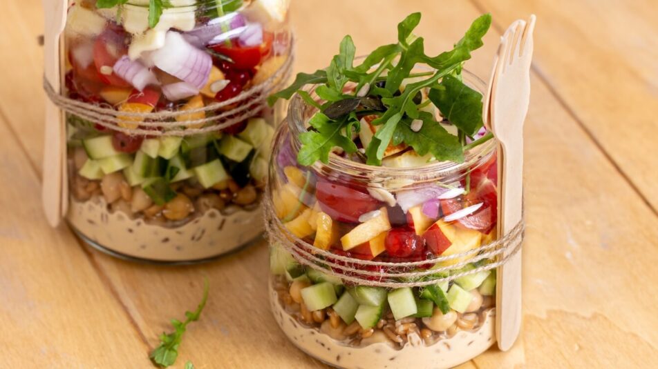 Bunter Salat im Glas mit frischem Gemüse und Rucola, ideal für ein Picknick. Die Gläser sind mit einer Schnur umwickelt und mit einer Holzgabel versehen.