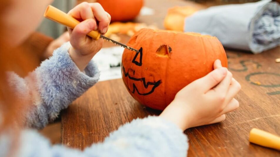 Kind schnitzt ein Halloween-Gesicht in Kürbis.