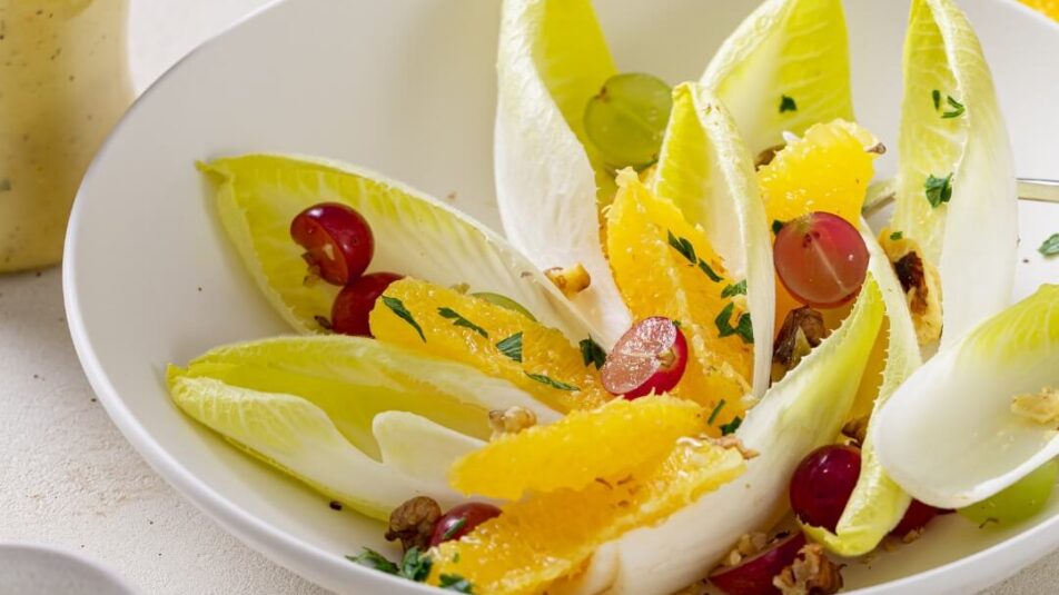 Winterlicher Salat mit Chicorée und Trauben in weissem Teller, daneben eine Flasche Salatsauce